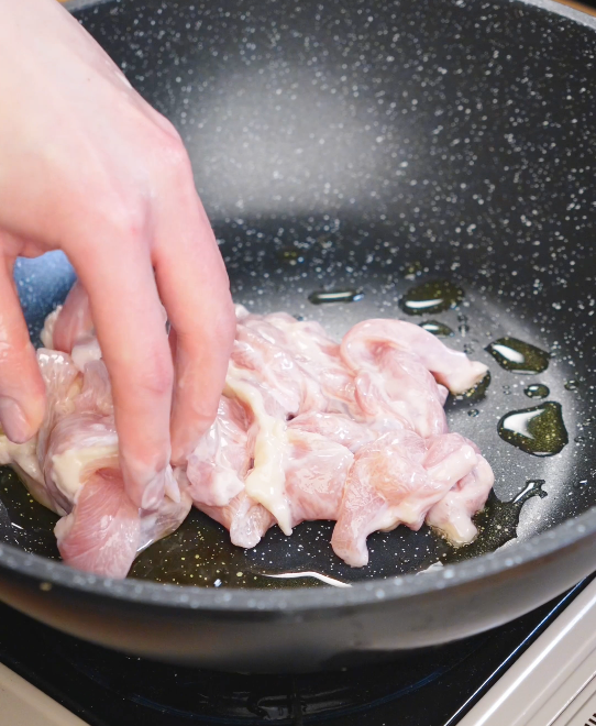 Marinated sliced chicken thighs being placed into a hot pan with oil to sear and cook before adding noodles for chicken chow fun.