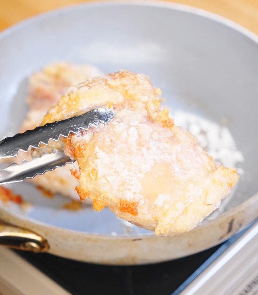 Golden crispy chicken thigh coated in cornstarch being lifted with tongs from a hot pan while frying for crispy garlic chicken.