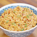Bowl of creamy peanut noodles garnished with sesame seeds, sliced scallions, and chili flakes.