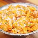 Bowl of Creamy Sausage Pasta topped with grated parmesan and chopped chives showing glossy orange cream sauce coating the rigatoni.