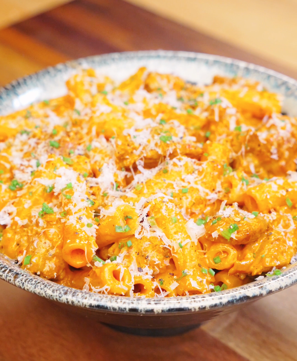 Bowl of Creamy Sausage Pasta topped with grated parmesan and chopped chives showing glossy orange cream sauce coating the rigatoni.