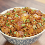 Bowl of garlic pork belly fried rice topped with scallions and crispy onions for extra flavor and texture.