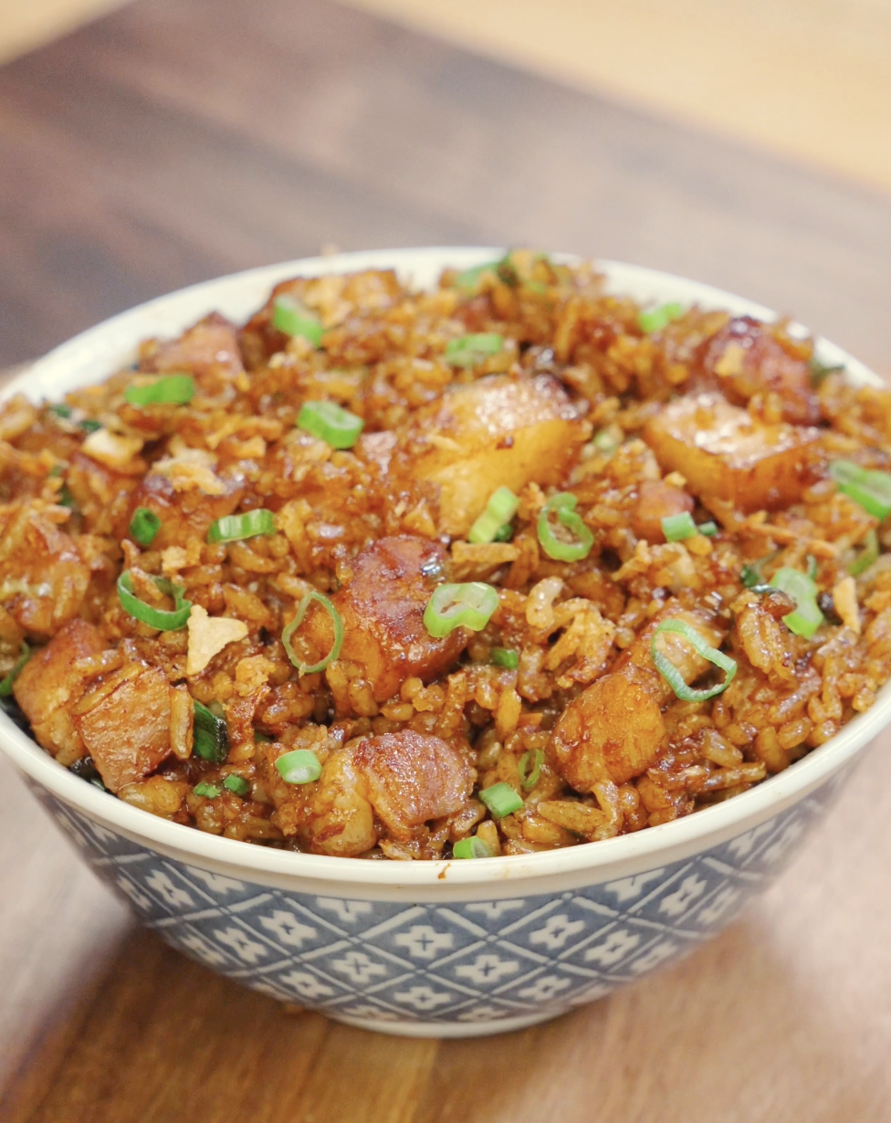 Bowl of garlic pork belly fried rice topped with scallions and crispy onions for extra flavor and texture.
