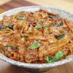 Bowl of garlic pork stir fry recipe with caramelized pork belly coated in glossy sauce and garnished with scallions.