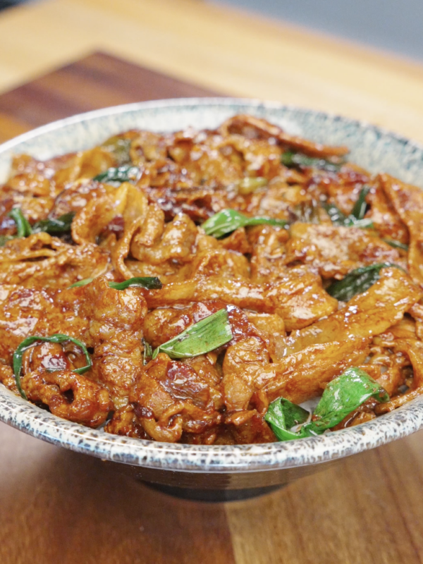 Bowl of garlic pork stir fry recipe with caramelized pork belly coated in glossy sauce and garnished with scallions.