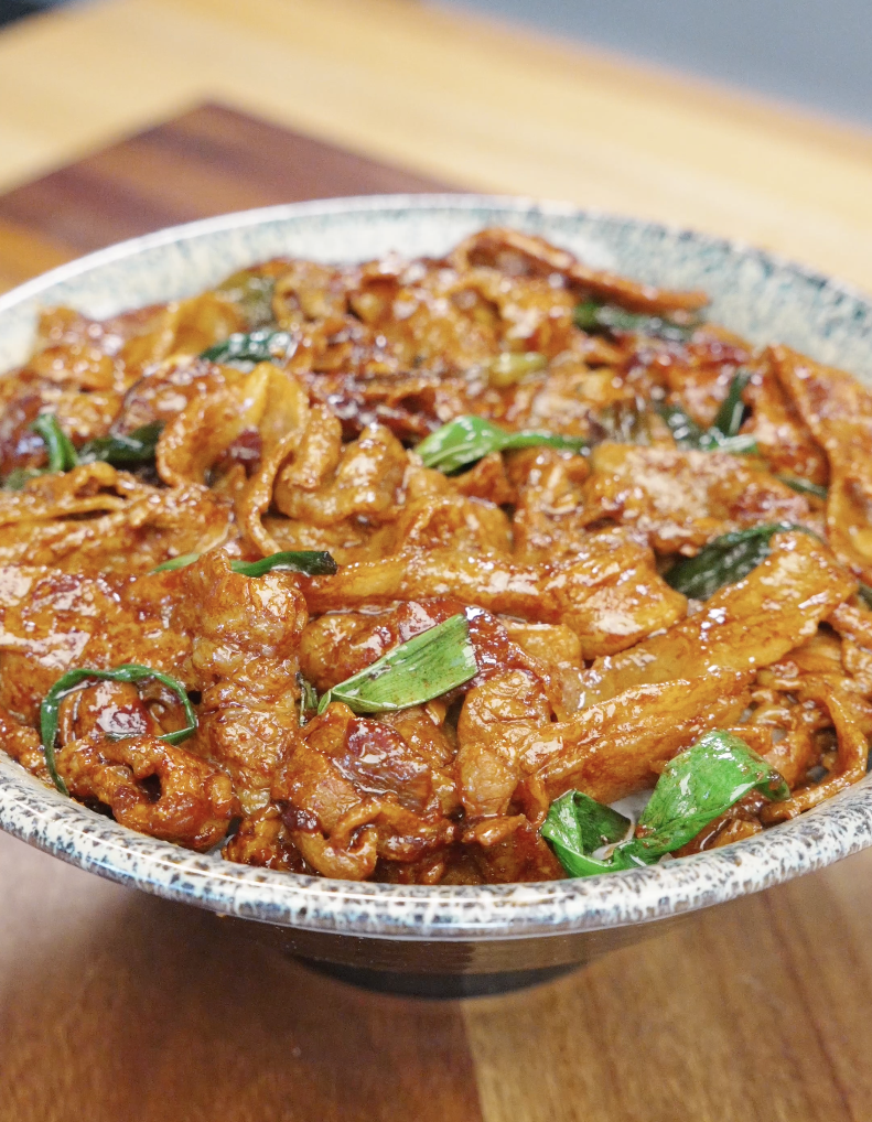 Bowl of garlic pork stir fry recipe with caramelized pork belly coated in glossy sauce and garnished with scallions.