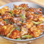 Bowl of honey garlic chicken stir fry with caramelized chicken, onions, garlic, and scallions served over steamed rice.