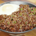 Bowl of Korean ground beef recipe served over rice with sesame seeds scallions and a fried egg.