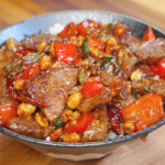 Bowl of Kung Pao Beef served over rice with red bell peppers, dried chilies, scallions, and roasted peanuts coated in kung pao sauce.