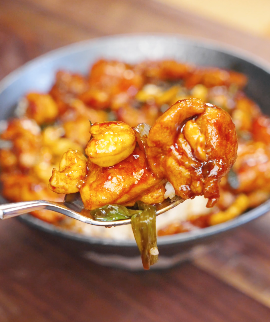 Fork lifting a bite of honey cashew chicken coated in sticky honey soy glaze with roasted cashews and scallions.
