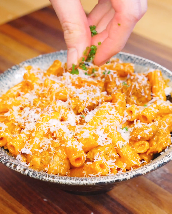 Hand sprinkling chopped chives over a bowl of Creamy Sausage Pasta topped with freshly grated parmesan and coated in a rich creamy sauce.