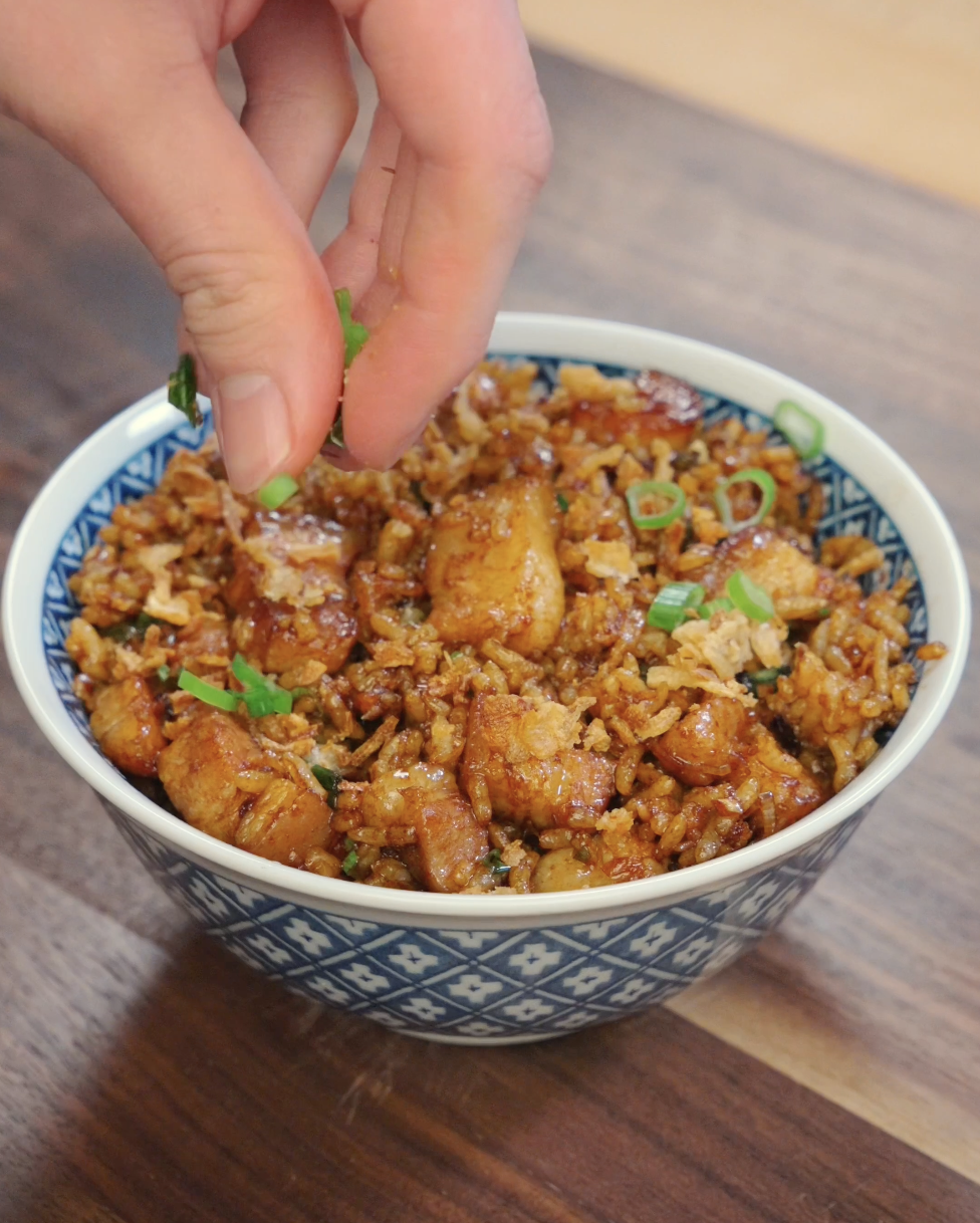 Fresh scallion greens being sprinkled over garlic pork belly fried rice while finishing the dish in the pan.