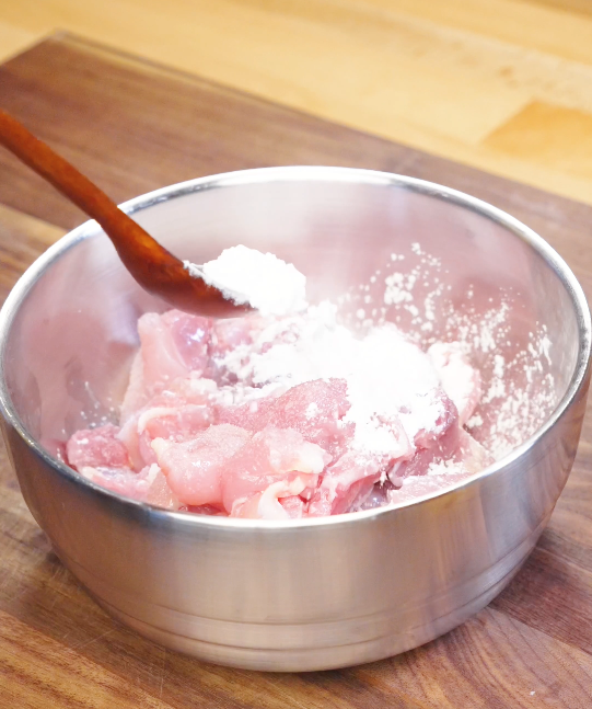 Cubed chicken thighs being coated with cornstarch, salt, and Shaoxing wine in a bowl to velvet the chicken before cooking honey cashew chicken.