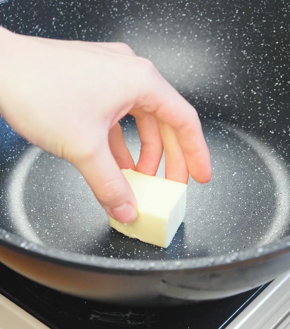 Cube of butter being placed into a hot pan to melt and form the base of the chili oil garlic butter noodle sauce.