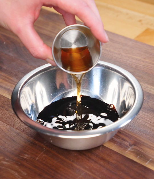 Dark soy sauce, light soy sauce, oyster sauce, Shaoxing wine, and sugar being poured together in a bowl to make chow fun stir fry sauce.
