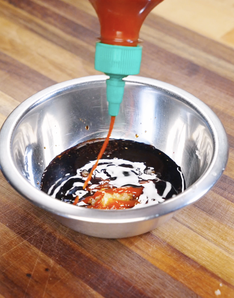 Dark soy sauce, light soy sauce, oyster sauce, honey, garlic, ginger, and sriracha being combined in a bowl for stir fry sauce.