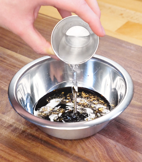 Water being poured into a bowl with dark soy sauce, light soy sauce, honey, rice vinegar, and chicken bouillon to create honey cashew chicken sauce.