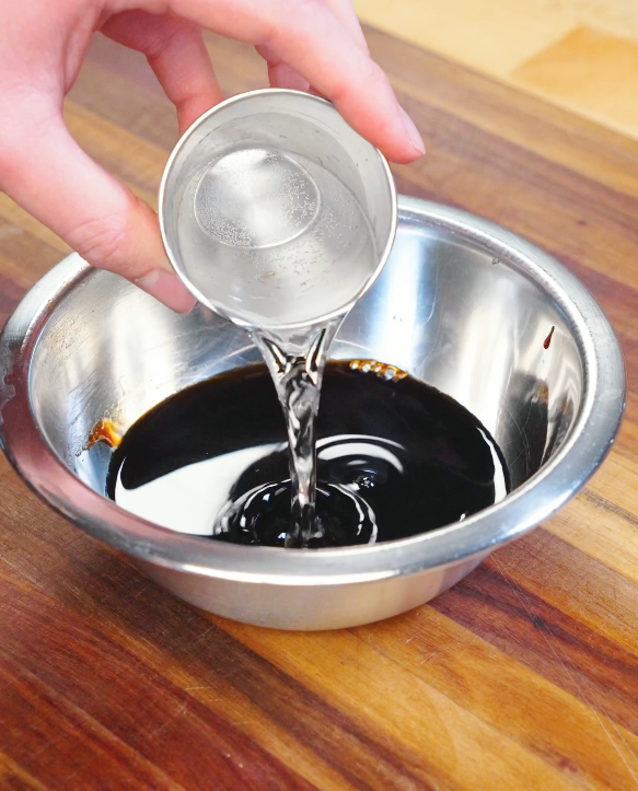 Water being poured into a bowl with soy sauce and other ingredients while preparing the sauce for Kung Pao Beef.