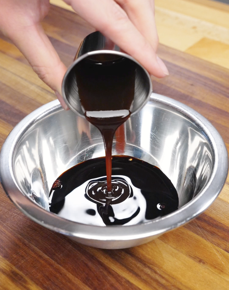 Dark soy sauce being poured into a metal bowl to create a rich savory sauce for garlic pork stir fry recipe.