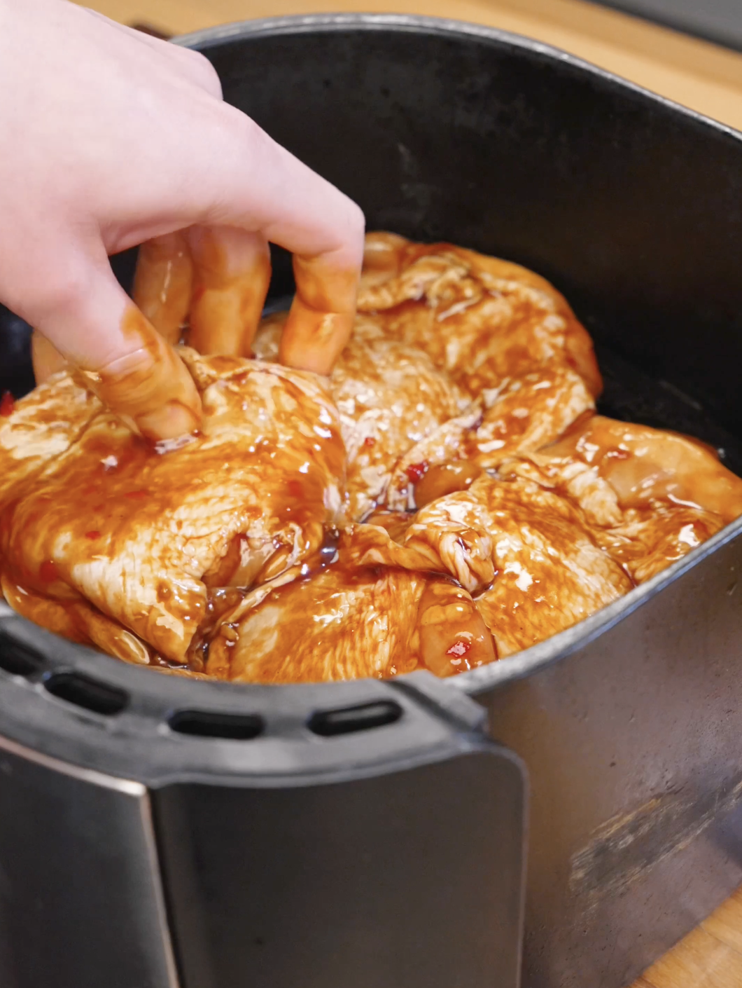 Hand arranging marinated chicken thighs inside an air fryer basket before cooking.