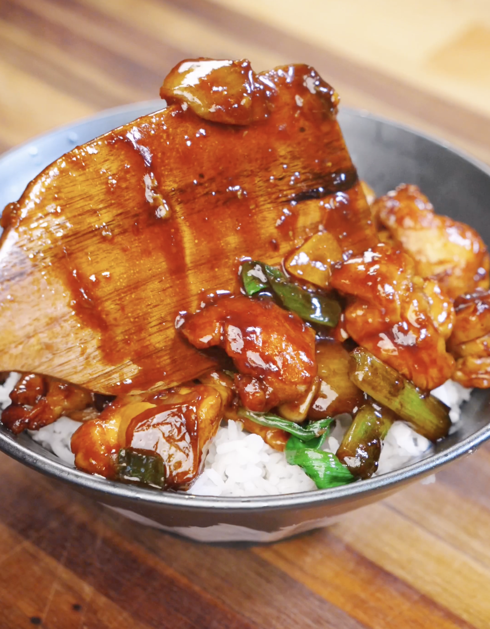 Wooden spatula placing Honey Garlic Chicken Stir Fry over a fresh bowl of steamed rice.