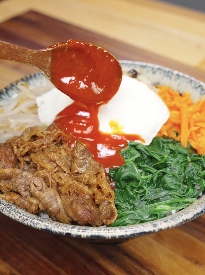 Spoon pouring gochujang sauce over rice beef and vegetables in a bowl for beef bibimbap recipe.
