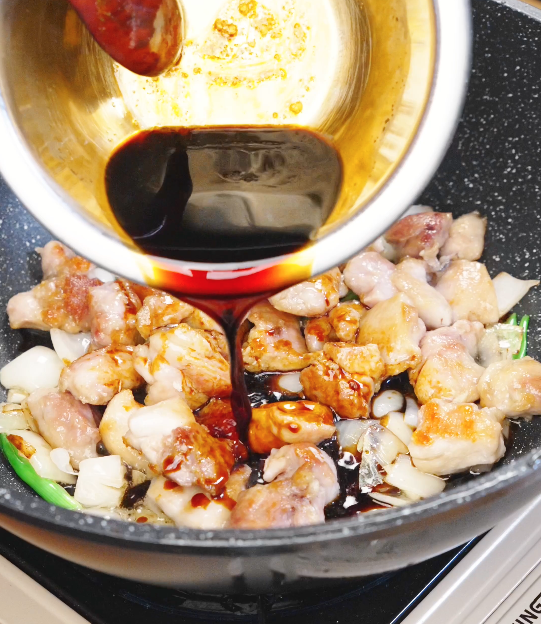 Thick honey soy sauce being poured over browned chicken and onions in a pan to glaze honey cashew chicken.