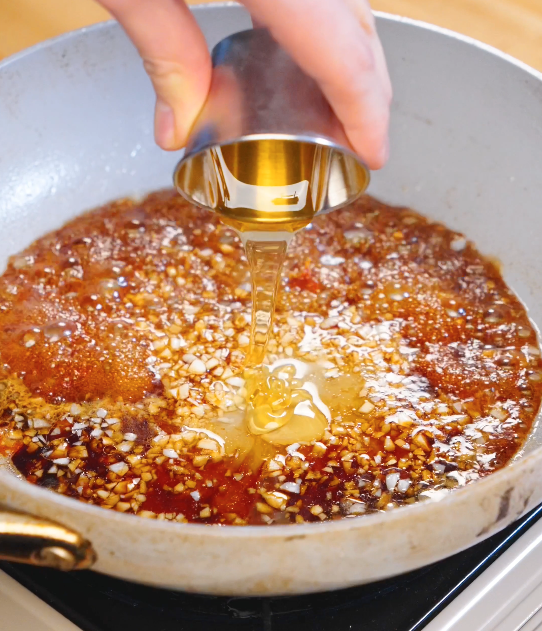 Honey being poured into a pan with soy sauce and minced garlic to create the sweet soy garlic glaze for crispy garlic chicken.