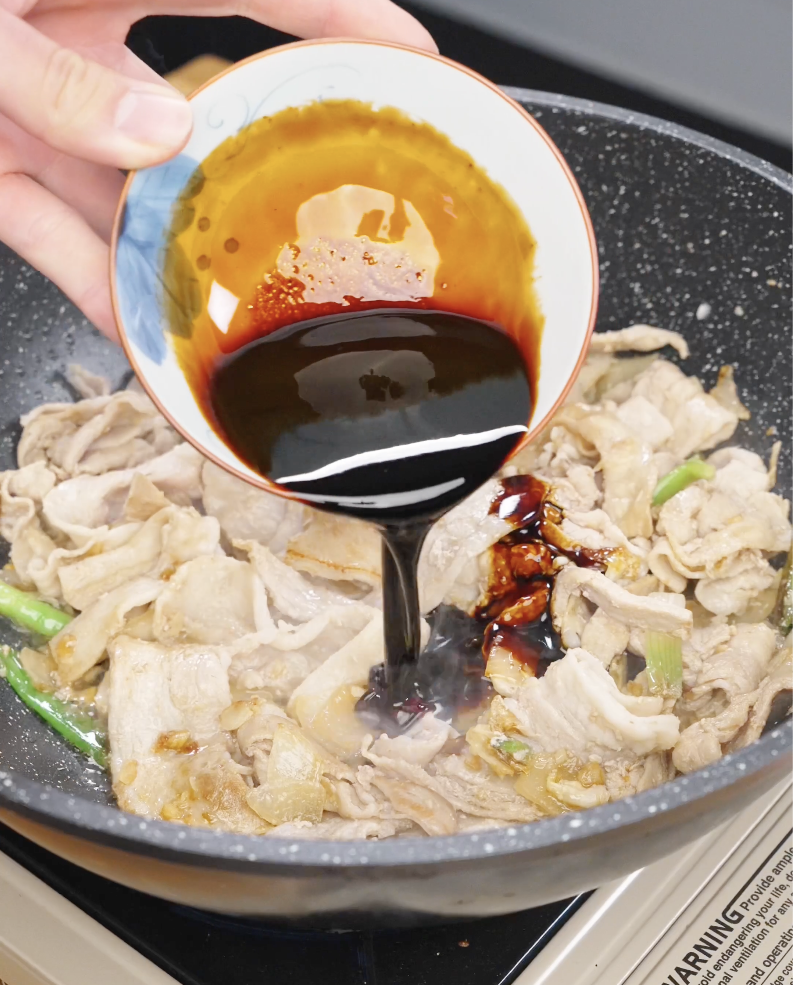 Thick garlic soy sauce being poured over pork belly in a pan to coat evenly in garlic pork stir fry recipe.