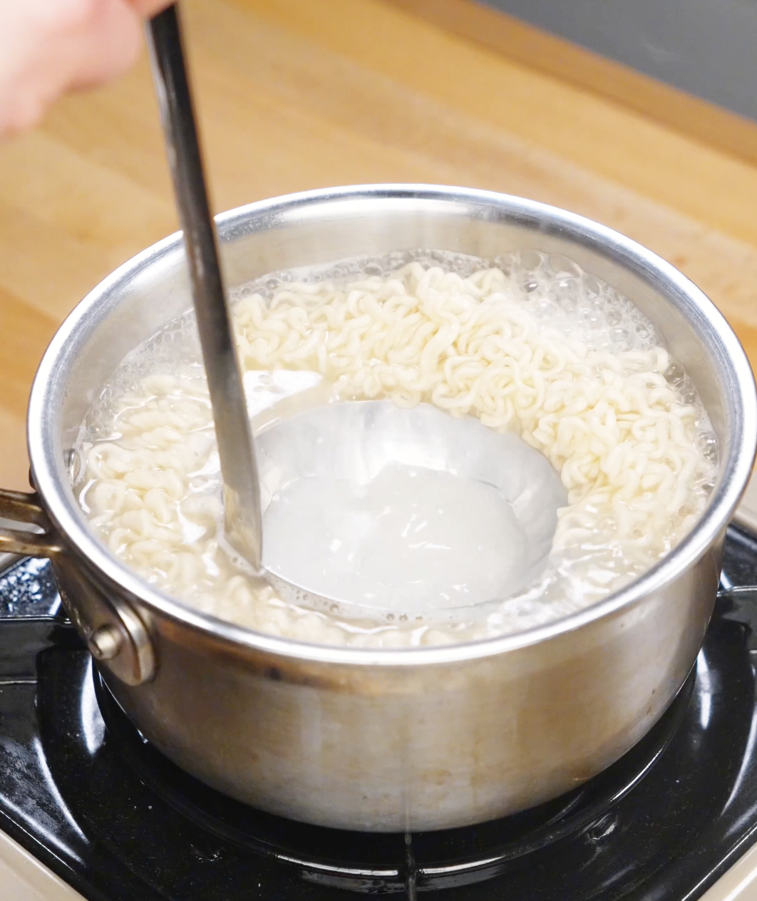 Ladle scooping starchy noodle cooking water from a pot of boiling ramen.