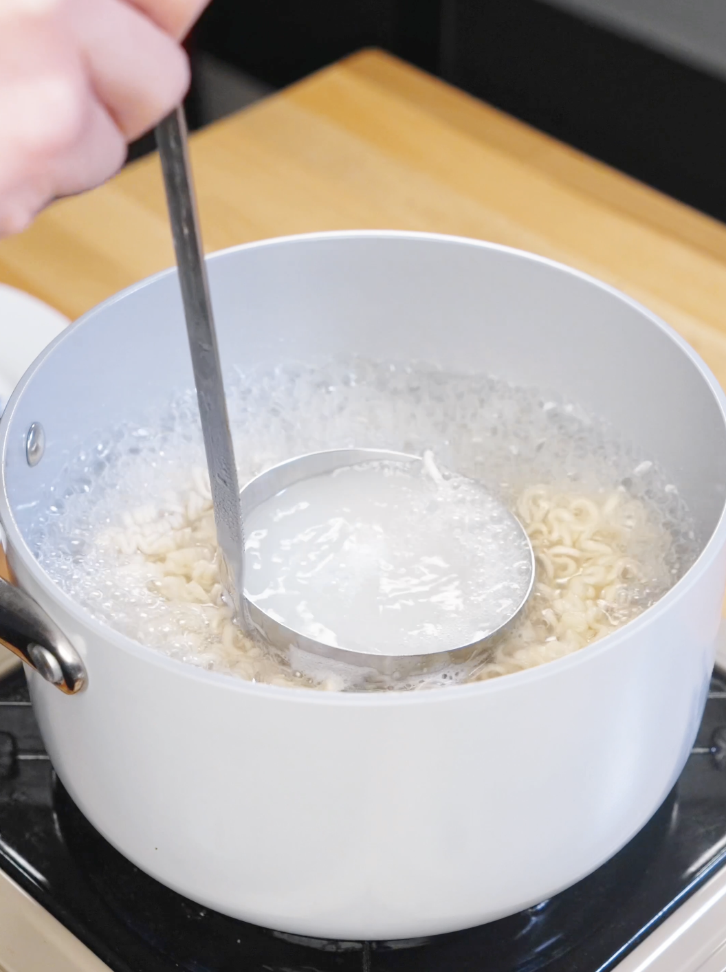 Ladle scooping cloudy noodle cooking water from a pot of boiling ramen noodles.