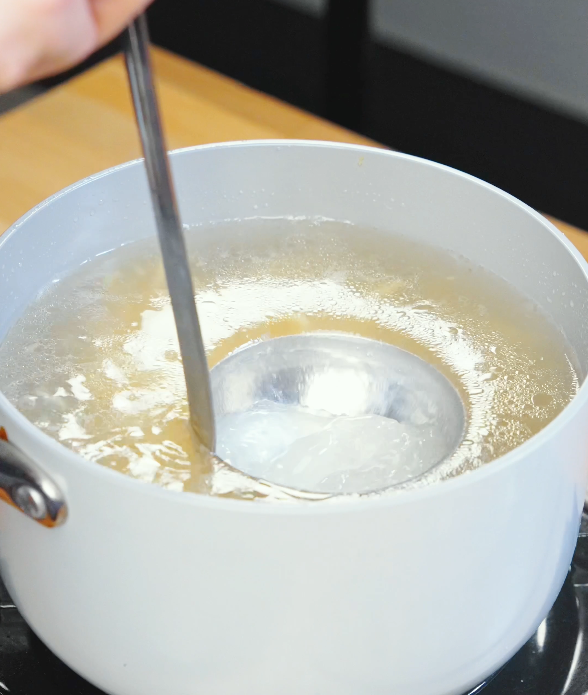 Ladle scooping reserved noodle cooking water from a pot to use for emulsifying chili oil garlic butter noodle sauce.