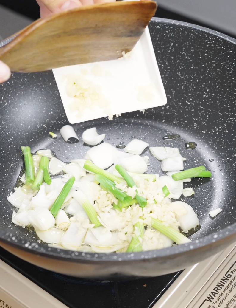 Chopped onions scallions and minced garlic cooking in oil to build the flavor base for garlic pork stir fry recipe.