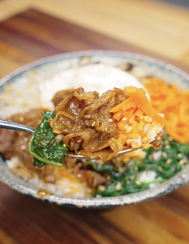 Spoon lifting a bite of beef bibimbap recipe with rice beef spinach carrots and gochujang sauce.