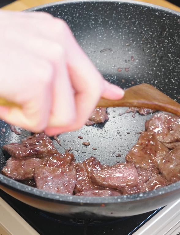 Thin slices of marinated beef searing in a hot pan while being stirred with a wooden spatula for Kung Pao Beef.