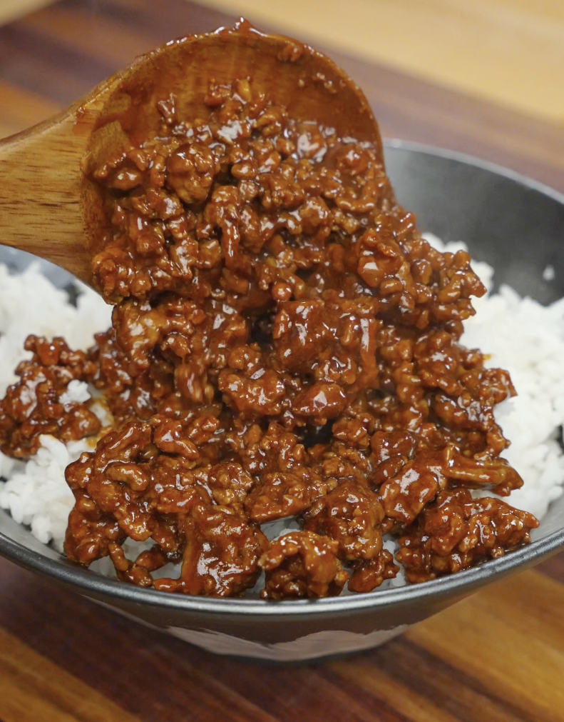 Cooked Korean ground beef being spooned over a bowl of white rice.