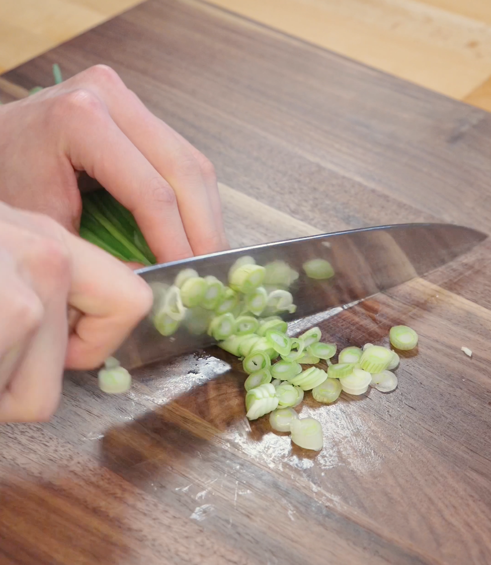 Fresh scallions being thinly sliced on a cutting board to prepare garnish and aromatics for garlic pork belly fried rice.
