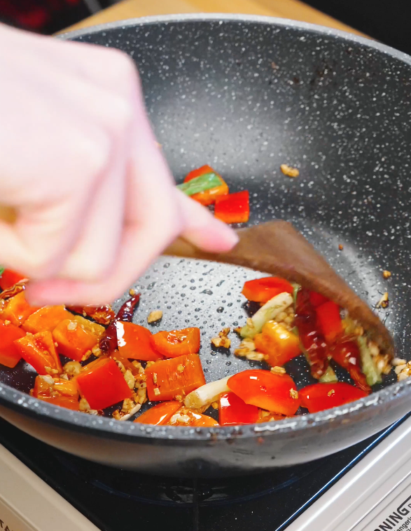 Red bell pepper pieces being stir fried with garlic and chilies in a pan as part of the cooking process for Kung Pao Beef.