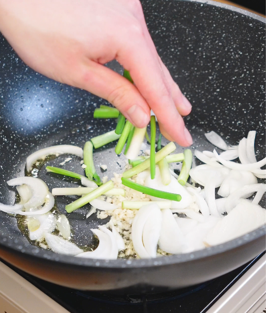 Garlic, sliced onions, and scallion whites saut&eacute;ing in a hot pan to build the aromatic base for chicken chow fun.
