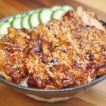 Sliced Sweet Chili Chicken served over steamed rice with sesame seeds and sliced cucumbers.