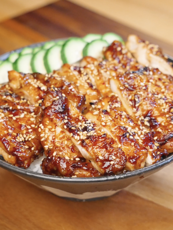 Sliced Sweet Chili Chicken served over steamed rice with sesame seeds and sliced cucumbers.