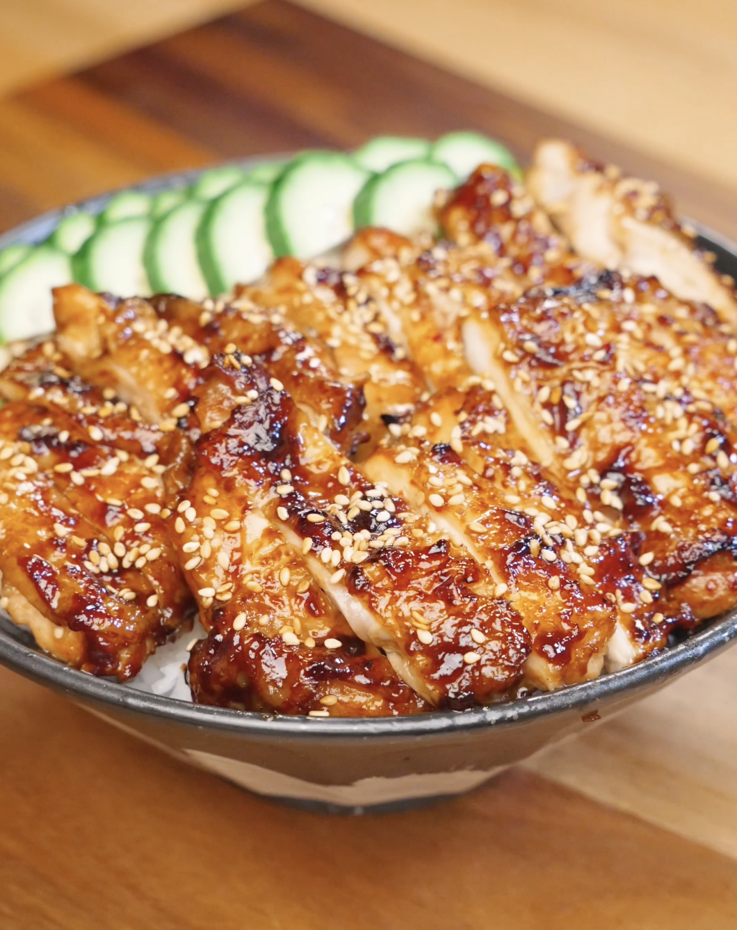 Sliced Sweet Chili Chicken served over steamed rice with sesame seeds and sliced cucumbers.