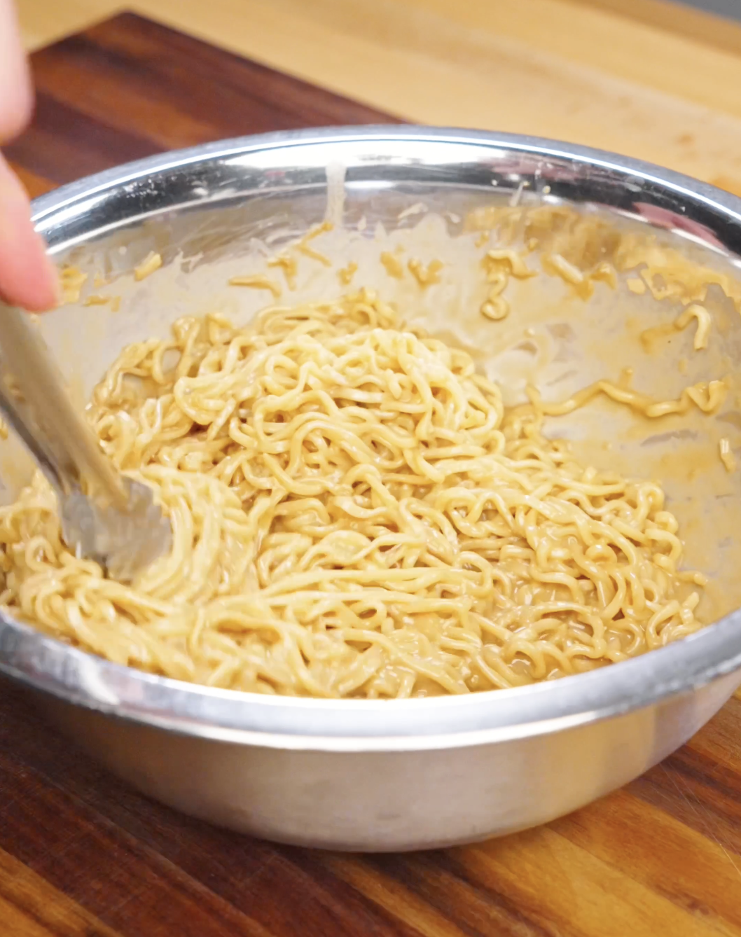Cooked noodles being tossed in a bowl with creamy sesame sauce until evenly coated.