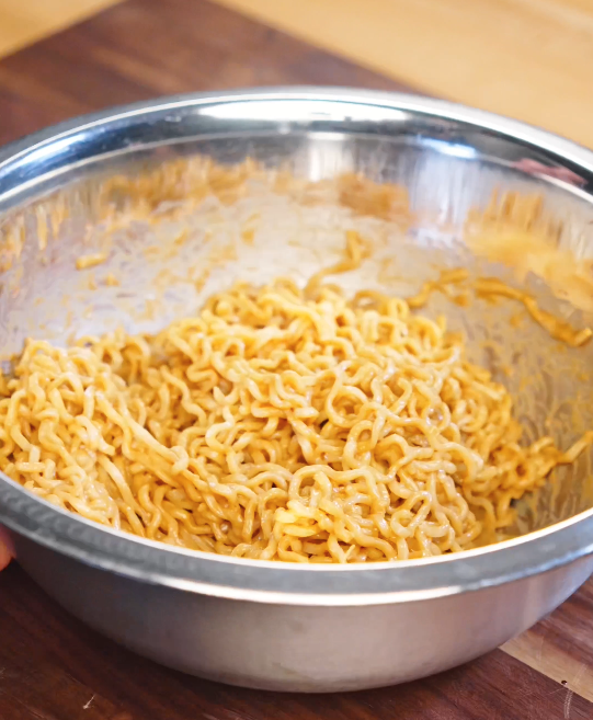 Cooked noodles being tossed in a large mixing bowl with creamy sesame garlic sauce until evenly coated.