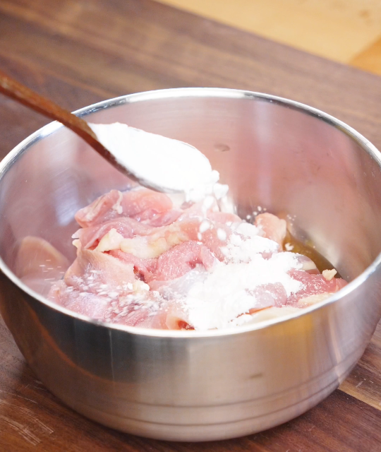 Thinly sliced chicken thighs in a bowl being coated with cornstarch, salt, and Shaoxing wine to tenderize the meat before stir frying.
