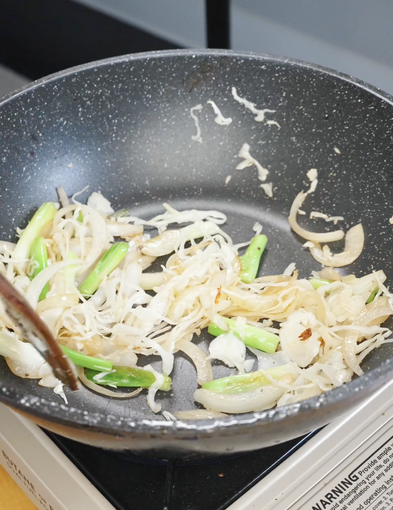 Shredded cabbage being added to saut&eacute;ed onions and scallions in a pan for the Beef Chow Mein Recipe.
