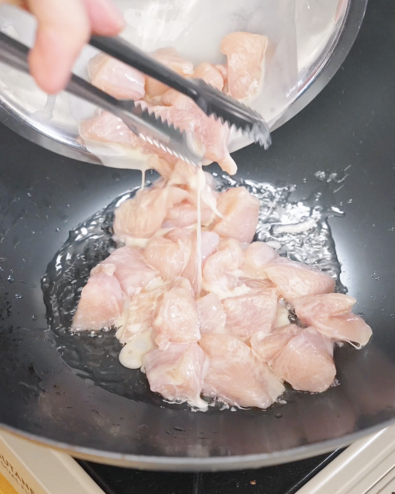 Marinated chicken pieces being placed into a hot pan with oil, starting the cooking process for chicken fried rice.