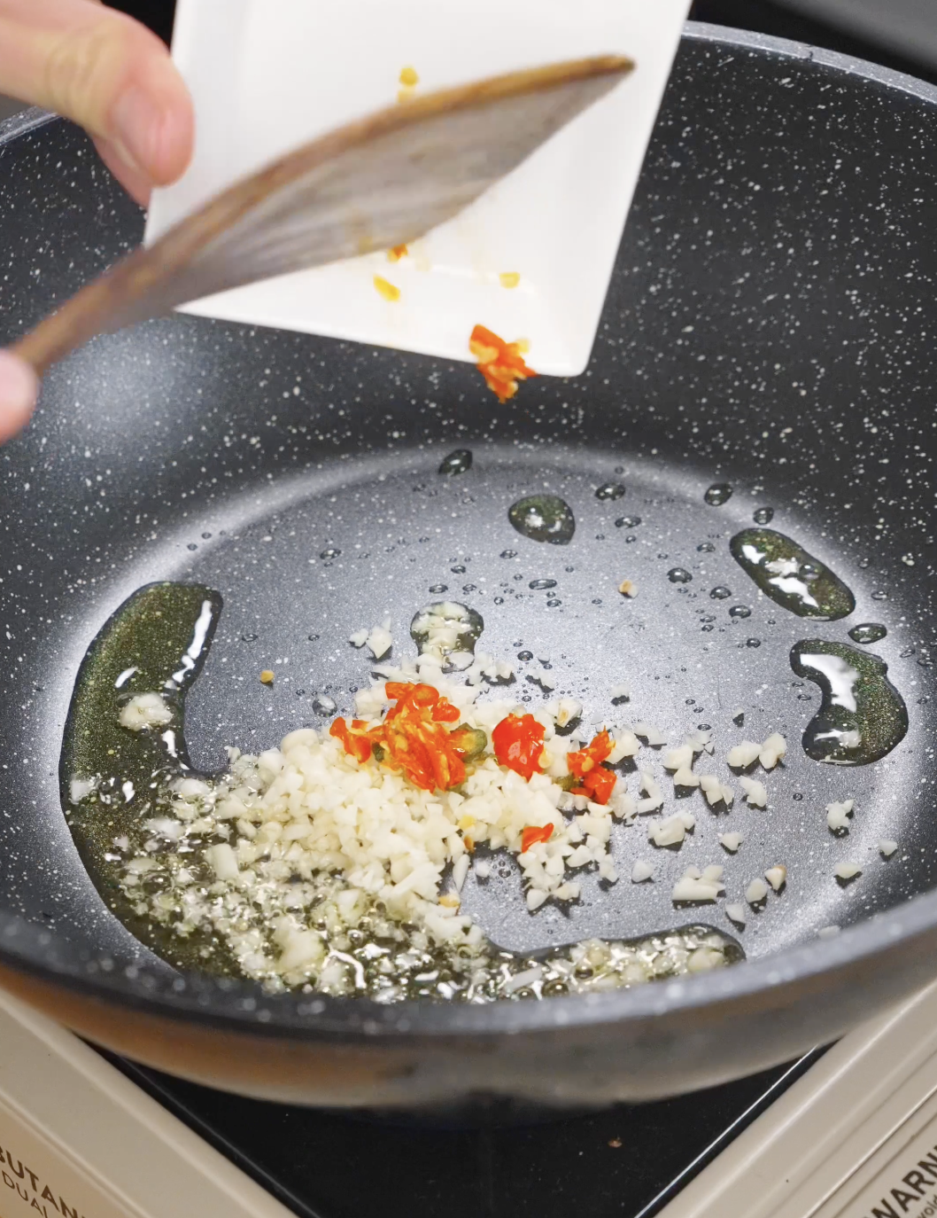 Minced garlic and chopped Thai chilies being added to hot oil in a pan, building the aromatic base for Thai basil ground beef.