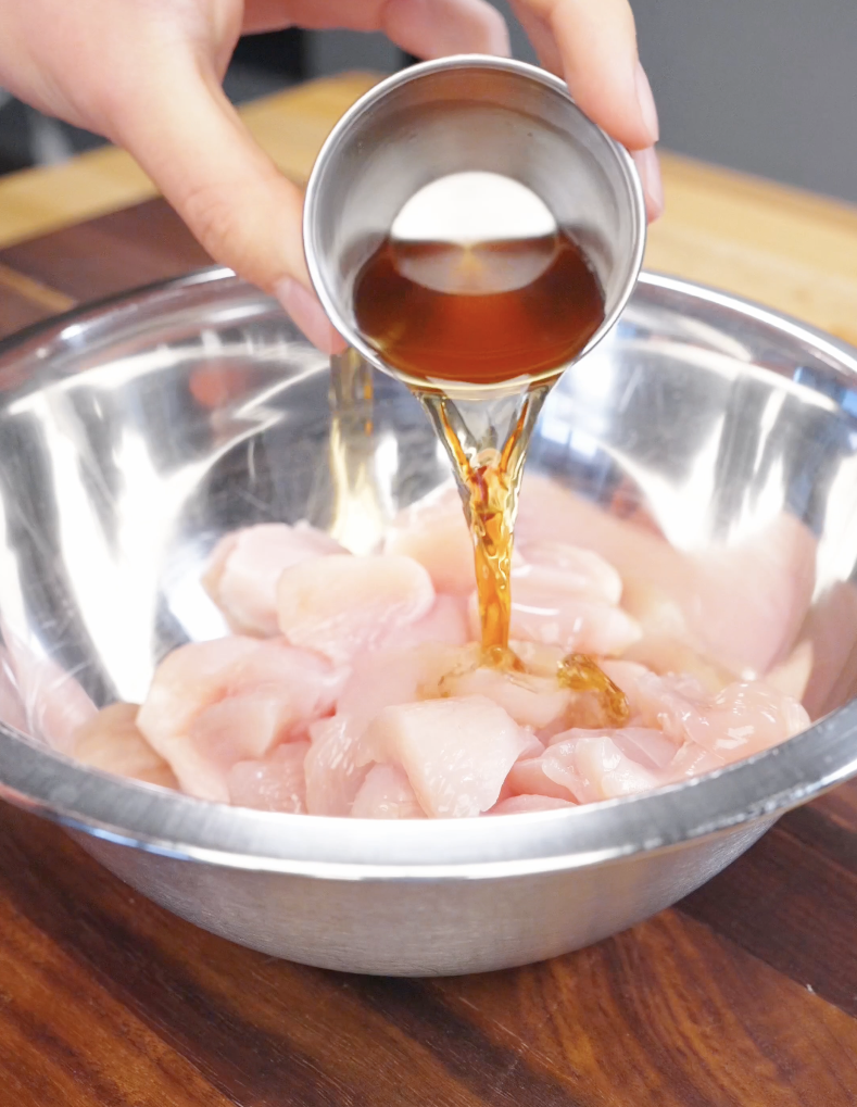 Shaoxing wine being poured over cubed raw chicken in a bowl, marinating the chicken for fried rice.