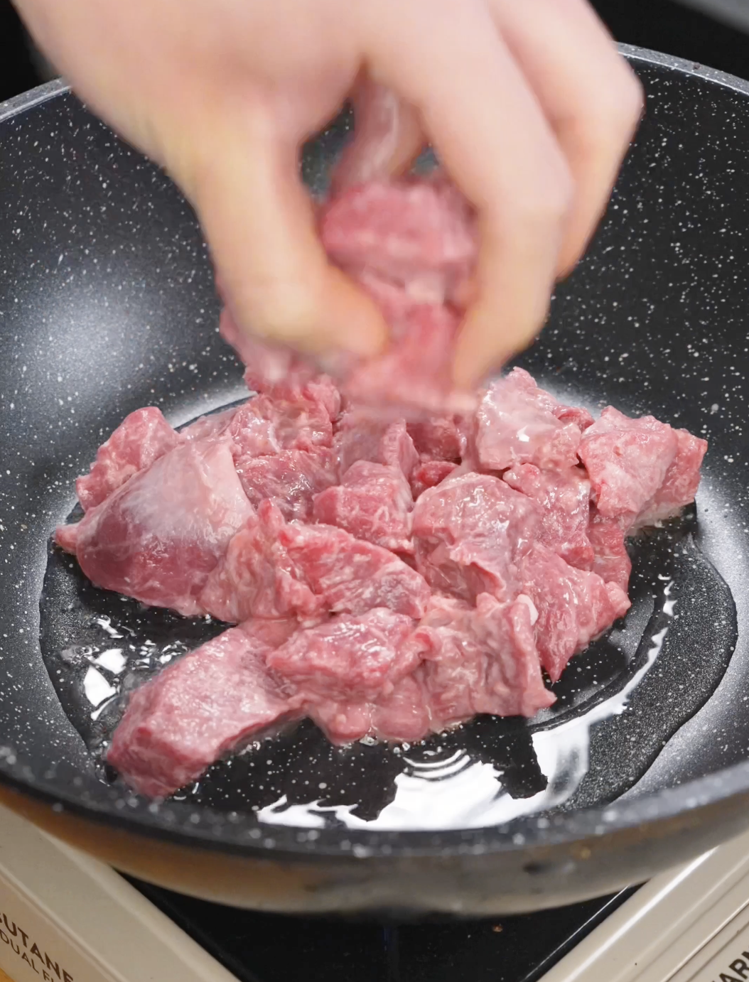 Marinated cubed sirloin beef being placed into a hot pan with oil, beginning the searing process to develop a browned crust for garlic beef fried rice.